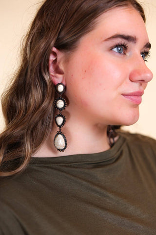 Model showcasing Along The Trail Cream Howlite Rock Copper Dangle Earrings by GRACE+EMMA, featuring a unique design with cream howlite stones and copper accents, perfect for elevating any outfit.